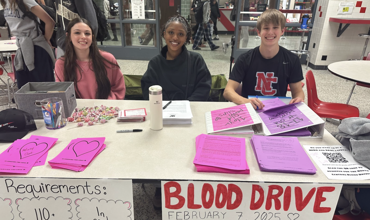 Senior class council officers (left to right) Harper Moses, Jendayi Gymerah-Oliver, and Tobin Montgomery promote the blood drive during lunch periods. Students who signed up received a lollipop and a heart to hang on the blood drive sign in the stairs in K hall.